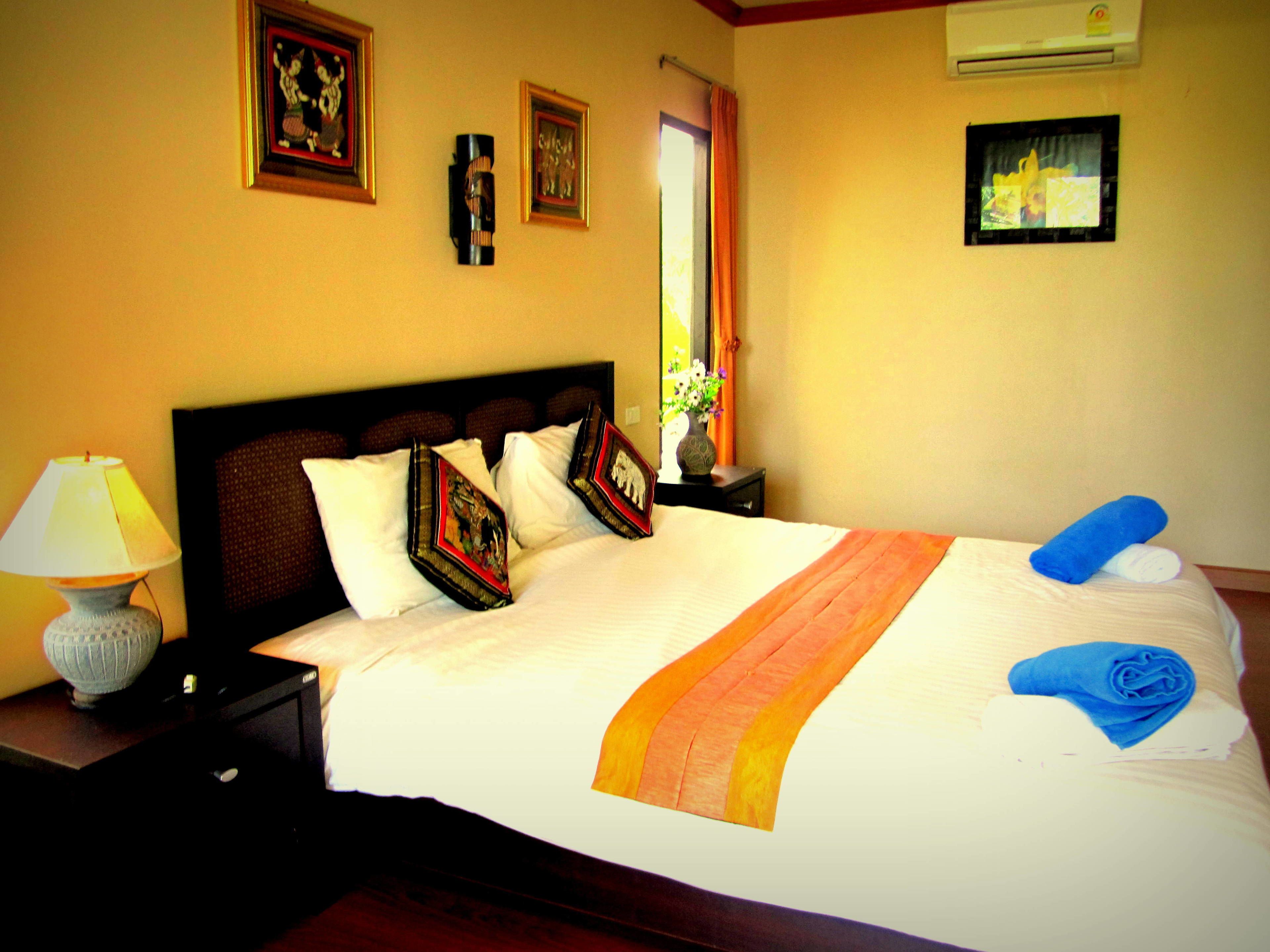Una cama bien hecha, con almohadas decorativas, una lámpara de noche y una toalla azul al lado.
