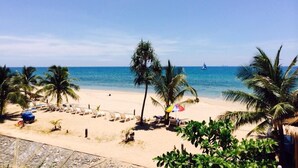 A beach with palm trees, lounge chairs, and a sailboat in the distance.