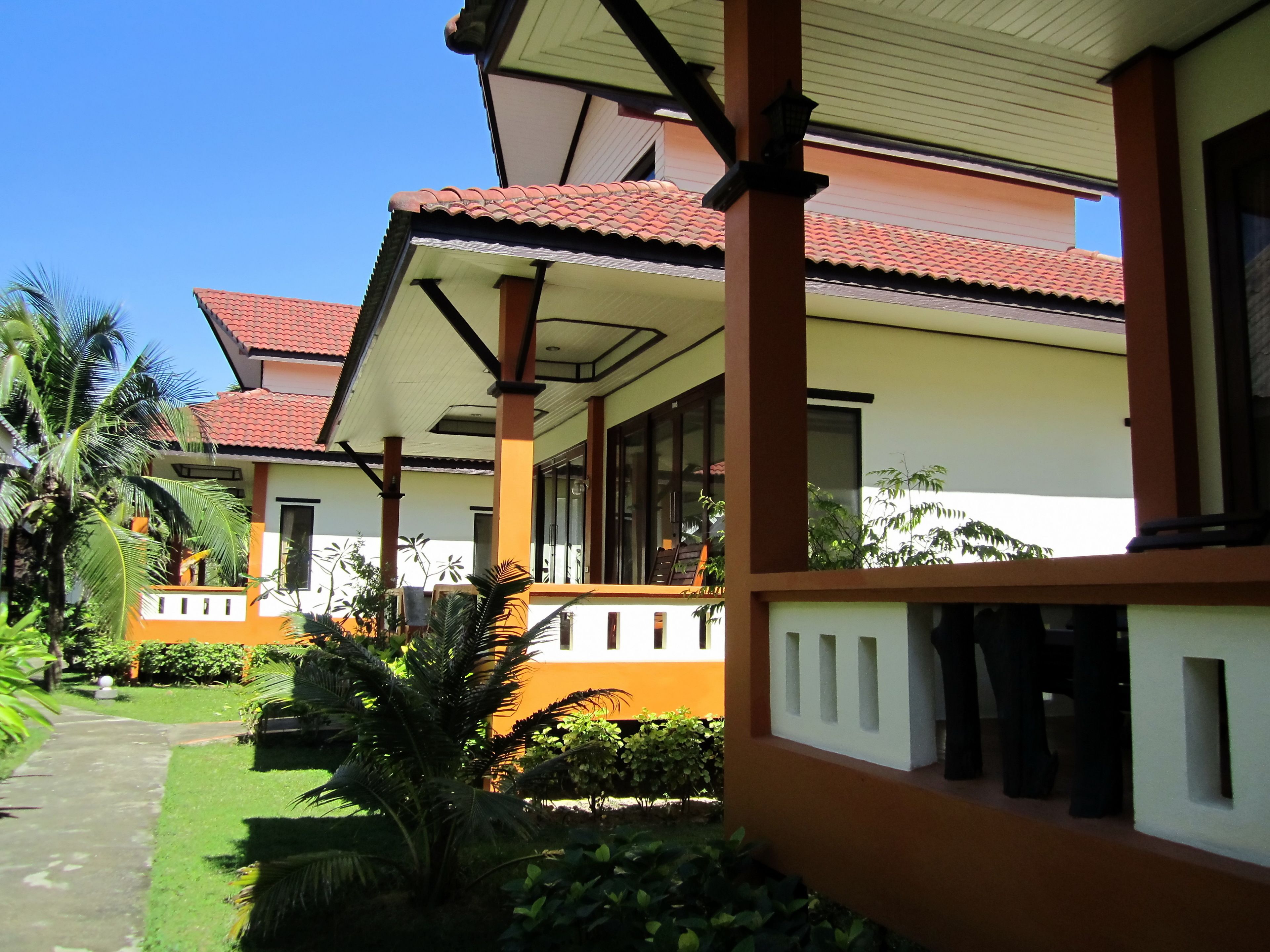 A two-story building with a red-tiled roof, a covered porch, and a well-maintained garden with palm trees.