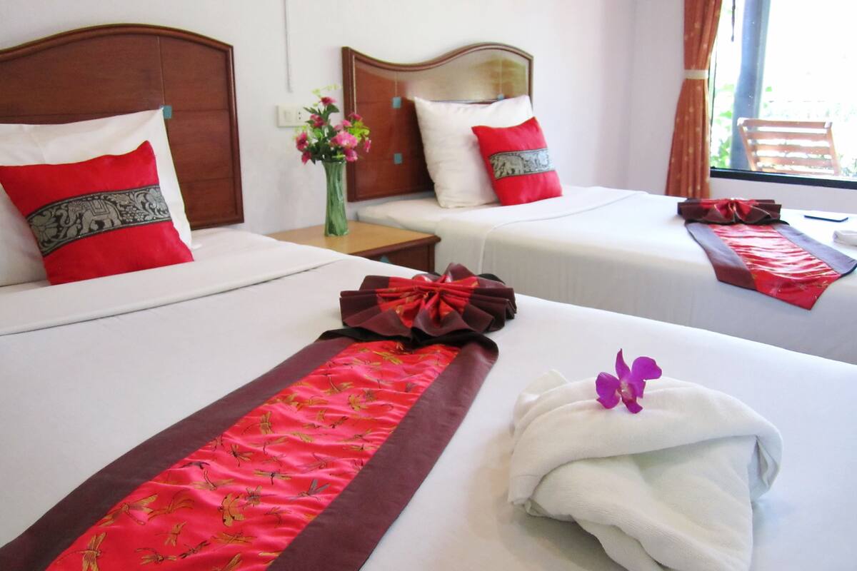Habitación de hotel con dos camas, cada una con almohada roja y blanca, un jarrón floral y un lazo rojo sobre las camas.