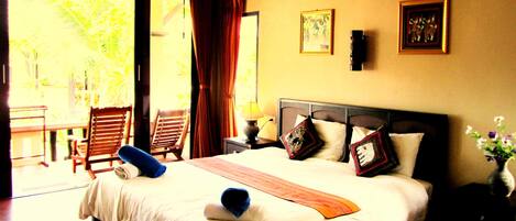 A hotel room with a bed, two chairs, a nightstand, and a window with curtains.