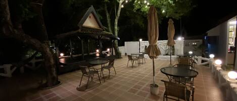 An outdoor patio area with tables and chairs, string lights, and a small gazebo.