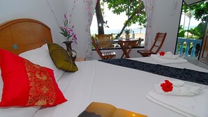 A hotel room with a bed, a view of the beach, and a table with chairs outside.