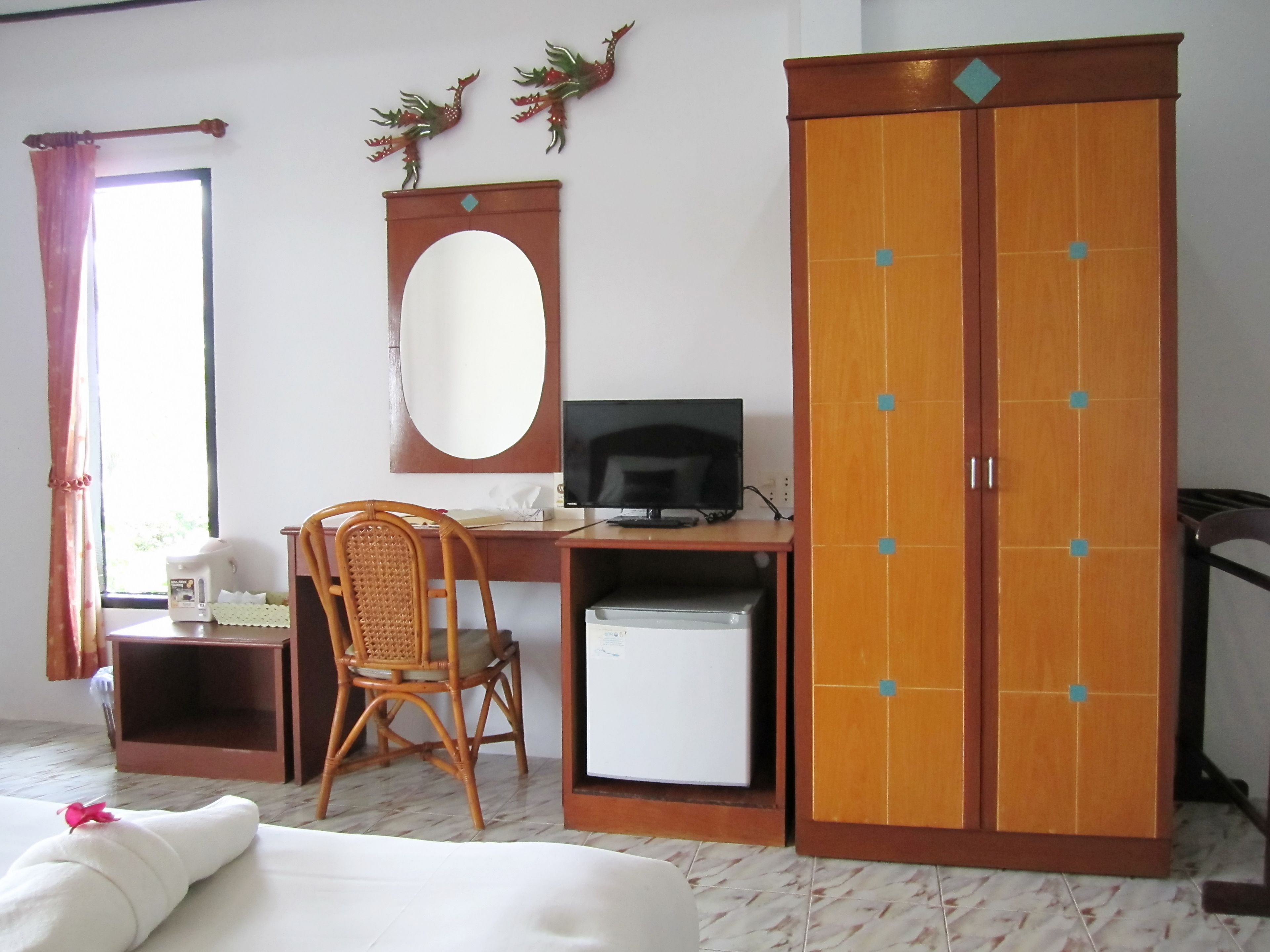A room with a bed, a desk with a computer, a chair, a wardrobe, a mirror, and a window with curtains.