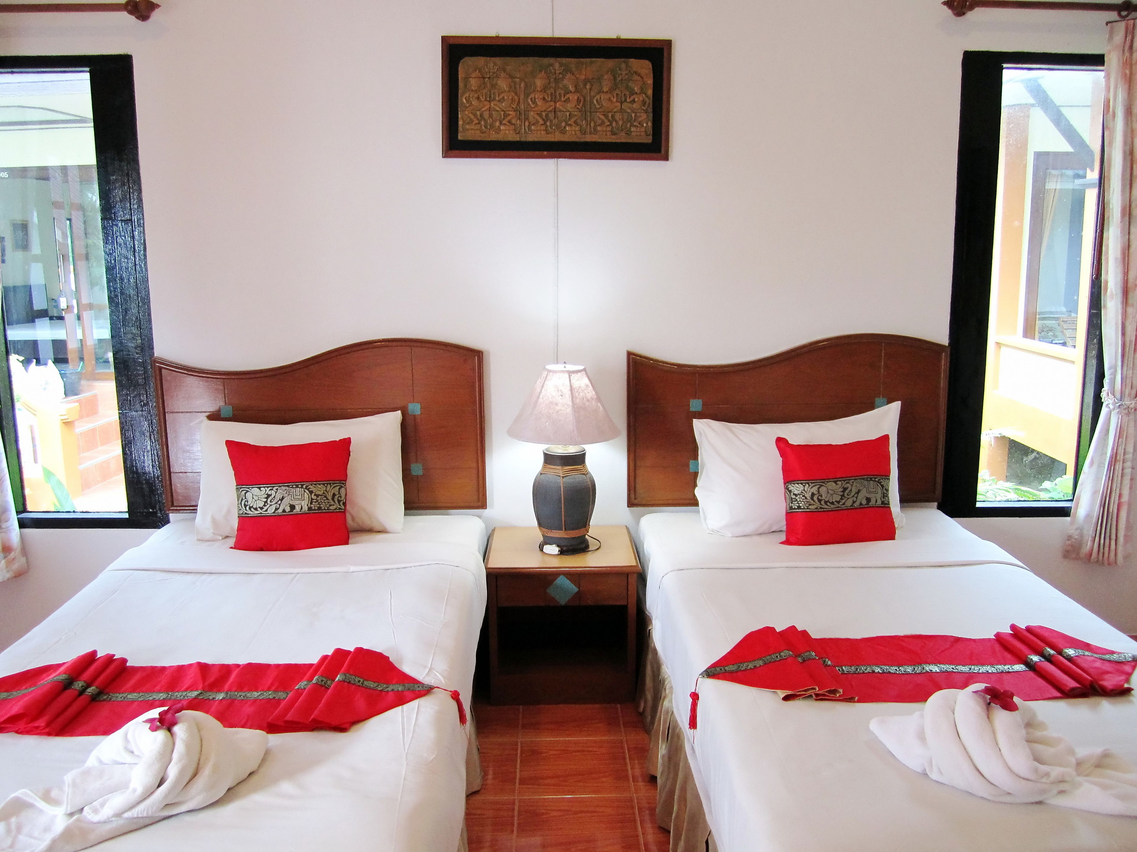A hotel room with two beds, each with red and white bedding, a wooden headboard, and a nightstand with a lamp.