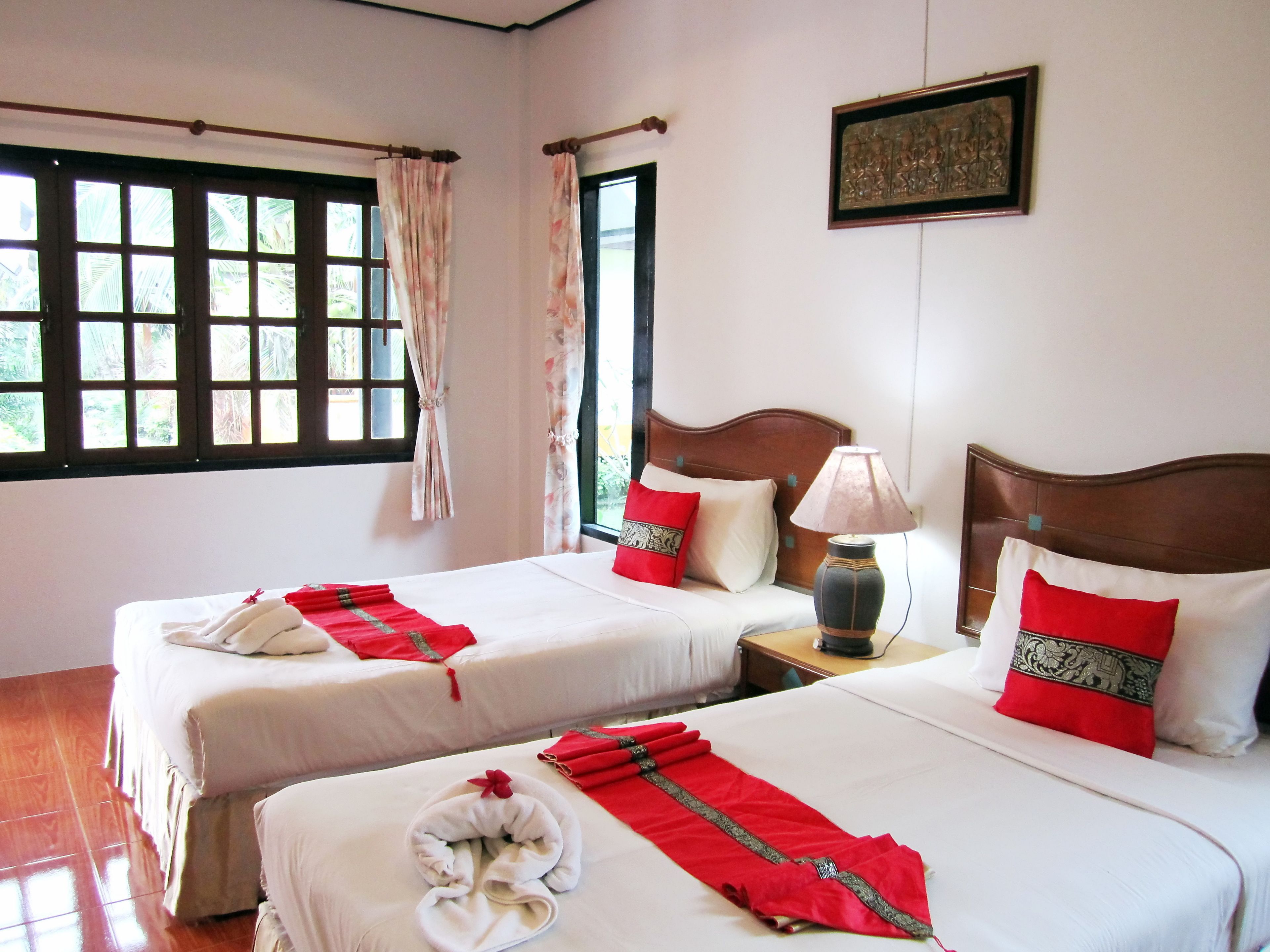 A hotel room with two beds, a nightstand with a lamp, and a window with curtains.