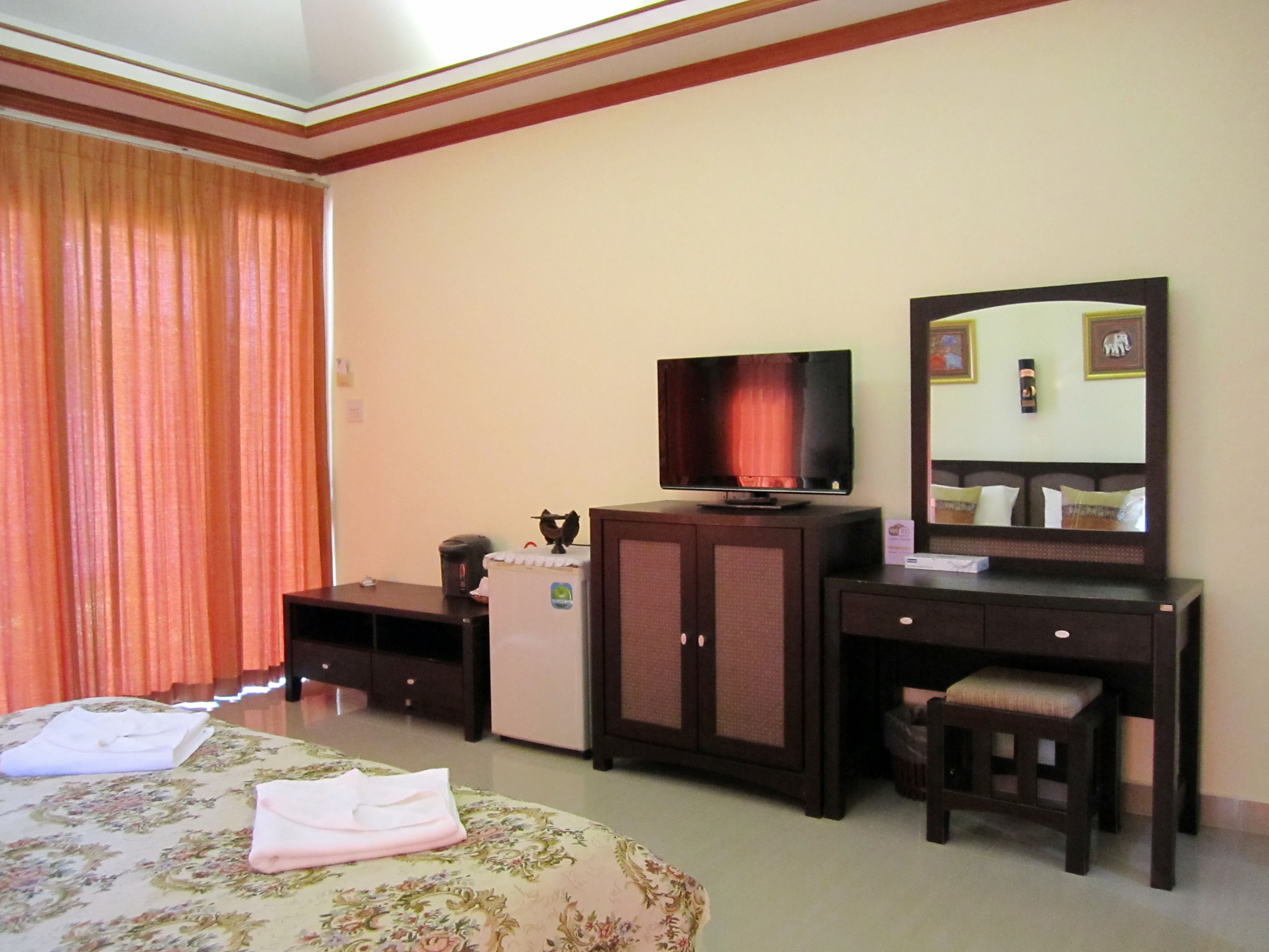 A hotel room with a bed, a television, a dresser, a mirror, and a small table.