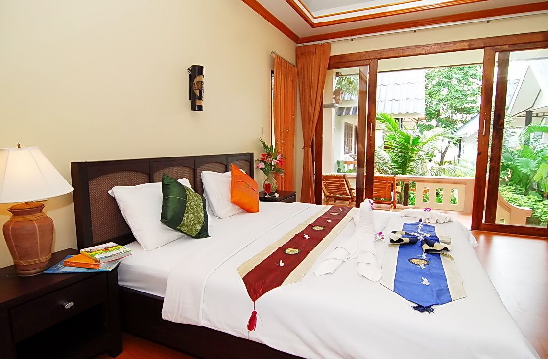 Une chambre d’hôtel avec un lit, une table de chevet avec une lampe, une fenêtre avec des rideaux et une vue sur la verdure.