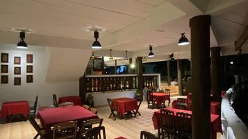 A restaurant with red tables and chairs, wooden beams, and hanging lights.