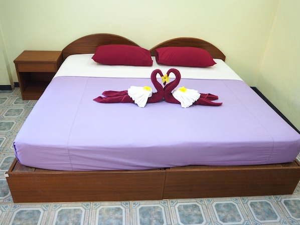 A neatly made bed with a purple bedspread, two red pillows, and a decorative swan made of fabric with yellow flowers.