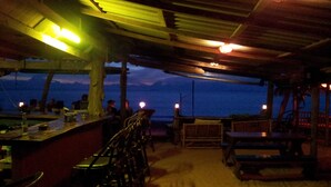 Un espace bar extérieur avec des meubles en bois et une vue sur la mer au crépuscule.