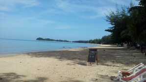 Une plage avec un panneau indiquant le prix du « Strawberry Margarita » à 100 bahts, des chaises de plage et une mer calme.
