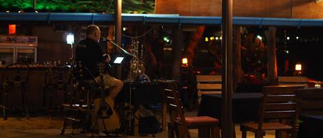 A musician performing at an outdoor venue with tables and chairs arranged for an audience.