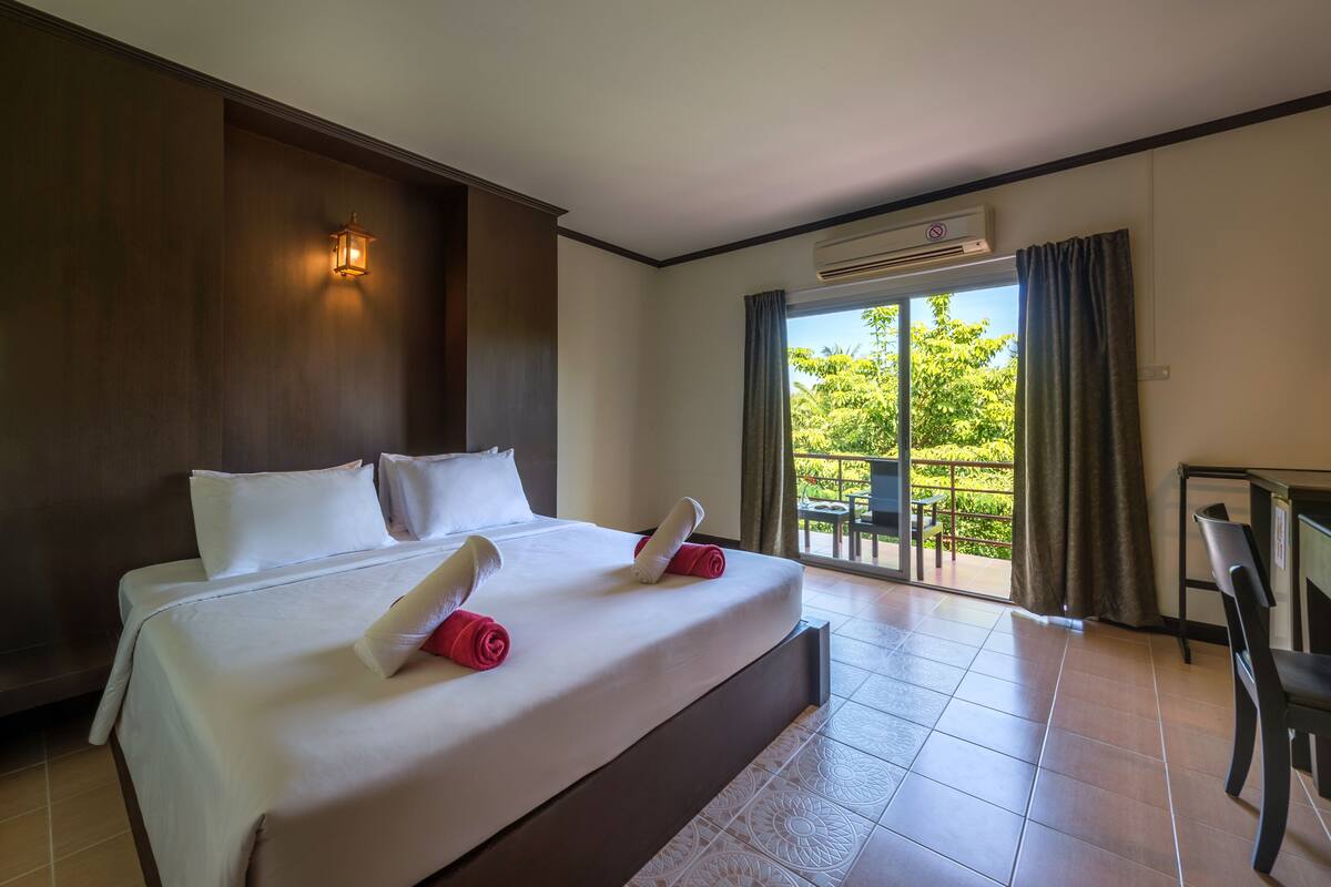Habitación de hotel con una cama grande, una lámpara de pared, un equipo de aire acondicionado y vistas a la vegetación a través de una puerta corrediza.