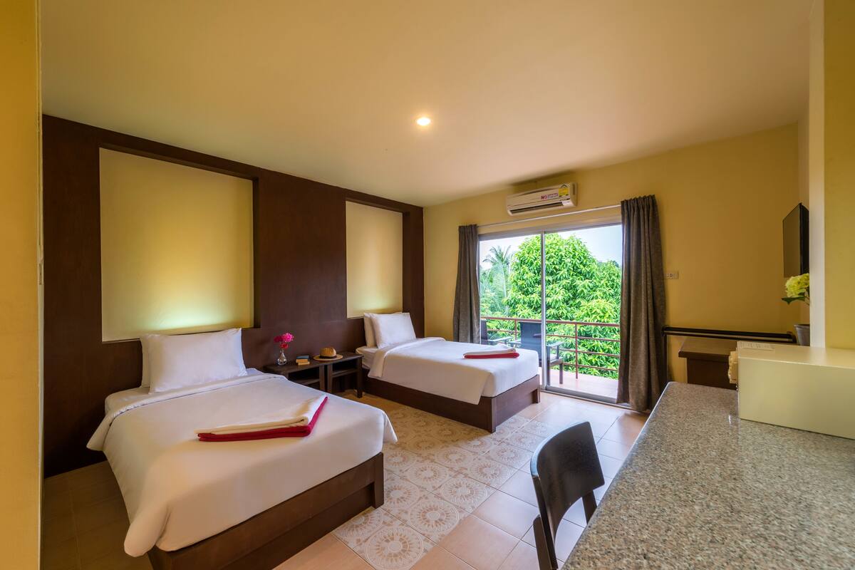 Habitación de hotel con dos camas, un escritorio y un balcón con vistas a zonas verdes.