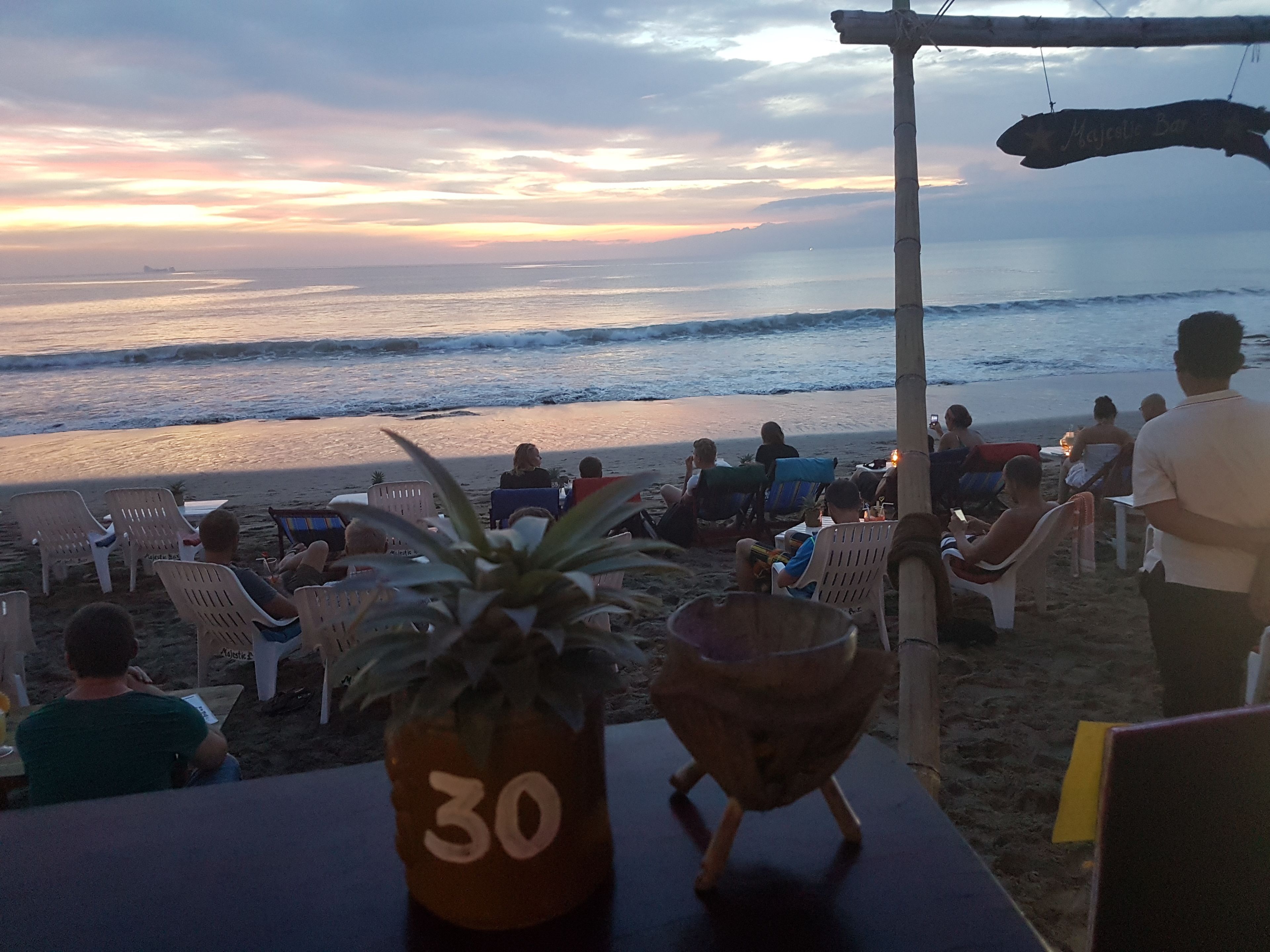 A beachside seating area with numbered chairs, a table with a plant, and a sign for Majestic Bar.