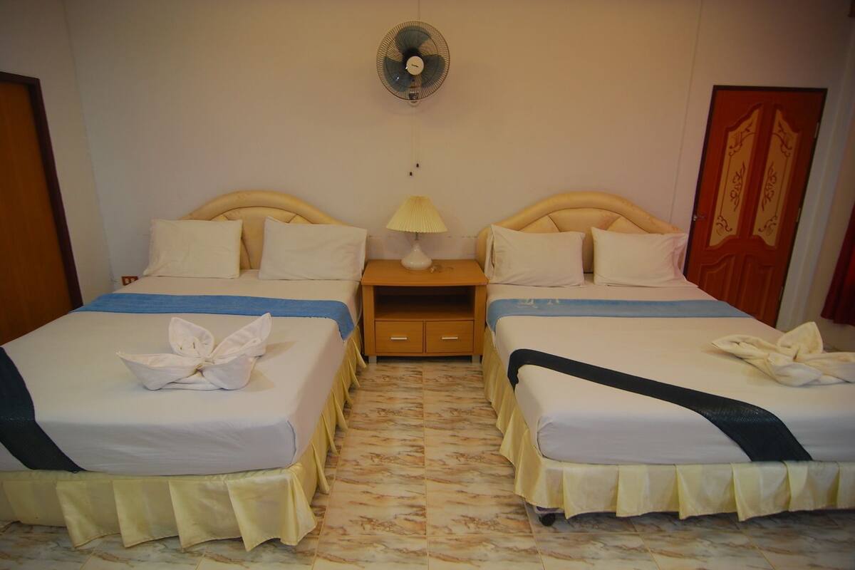 A hotel room with two beds, a nightstand with a lamp, a wall fan, and a door with decorative panels.