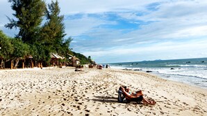 A beach with a couple relaxing on a lounge chair, surrounded by palm trees and beach huts. - Lanta Paradise Beach Resort (Ko Lanta)