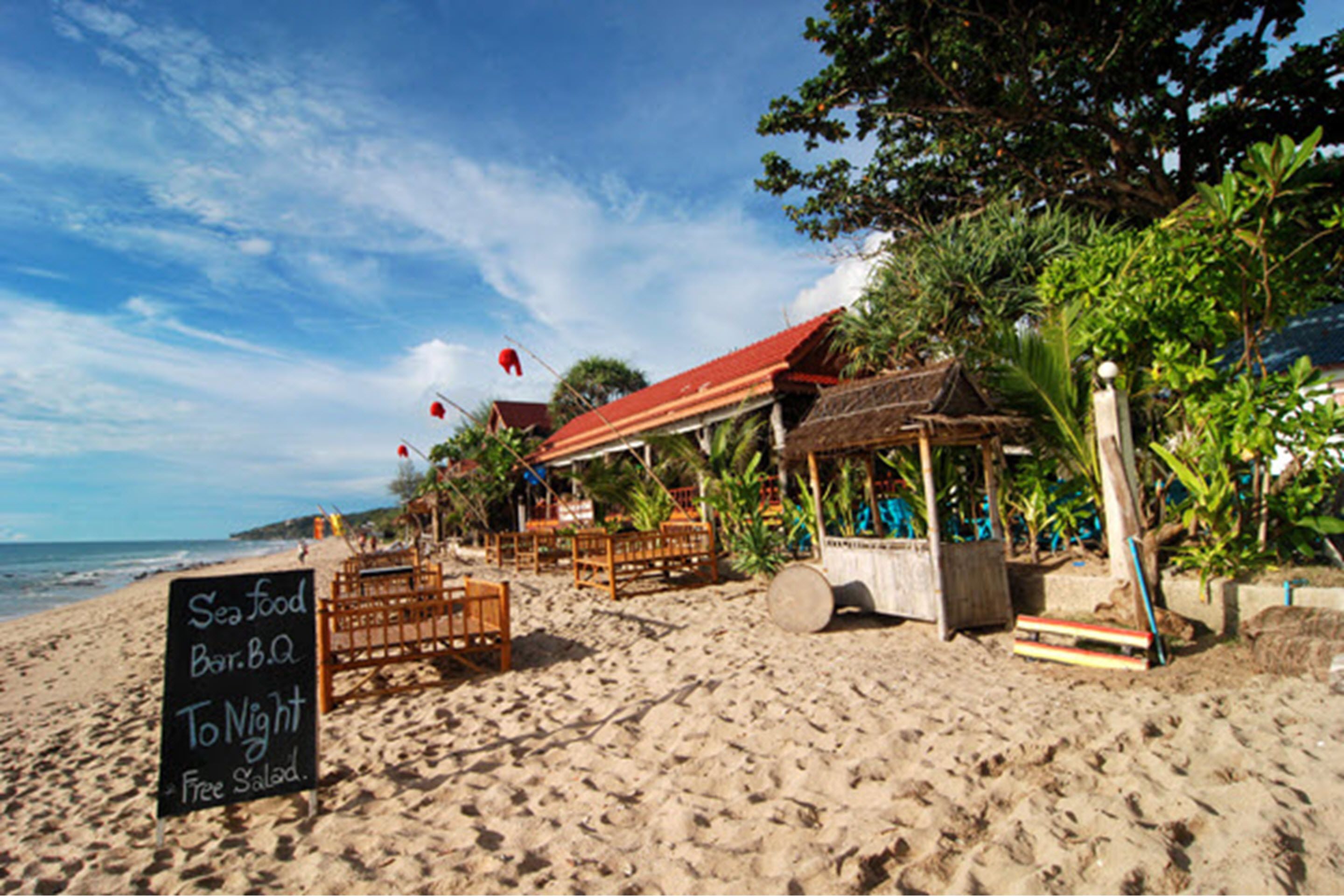 Un restaurant situé en bord de mer, avec une terrasse, une enseigne indiquant qu’il sert des fruits de mer et des plats grillés, et une vue sur l’océan.