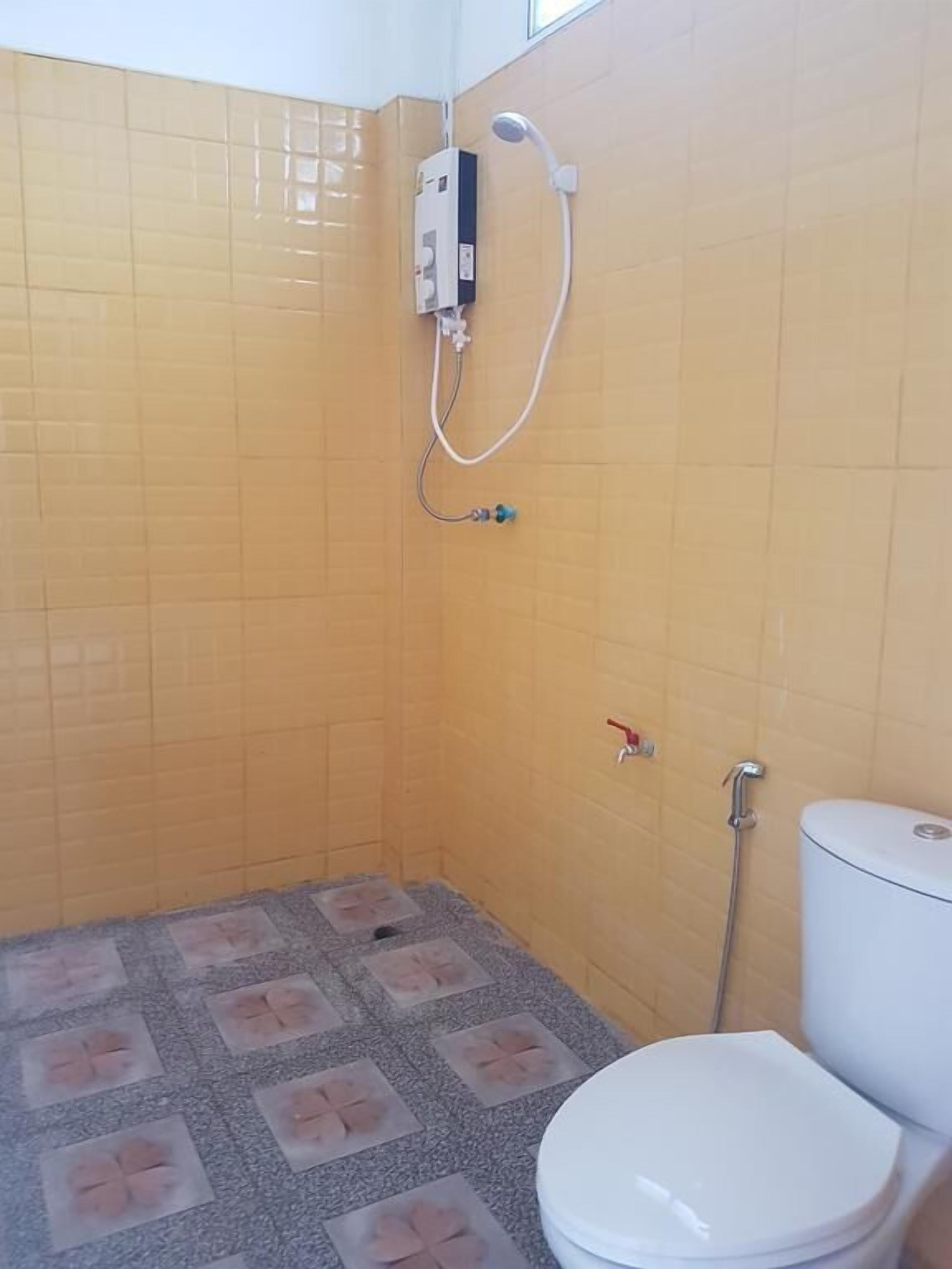 A small bathroom with yellow tiled walls, a white toilet, and a shower unit.
