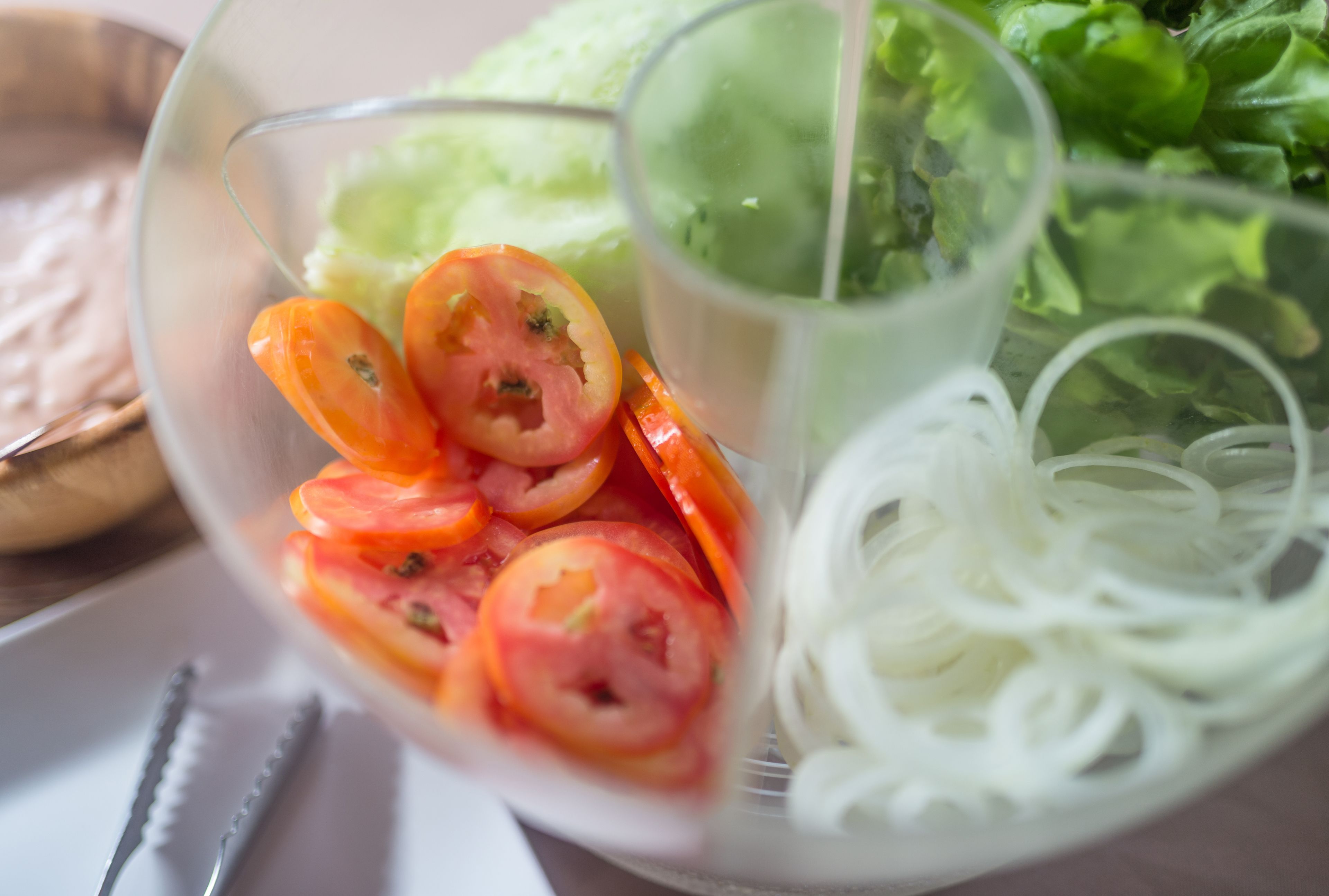 Uma tigela com fatias de tomate e macarrão, coberto por um líquido transparente, possivelmente um molho, sobre um prato branco.