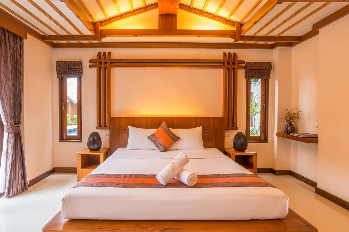 A large bed with a wooden headboard, two bedside tables, and a nightstand with a vase.