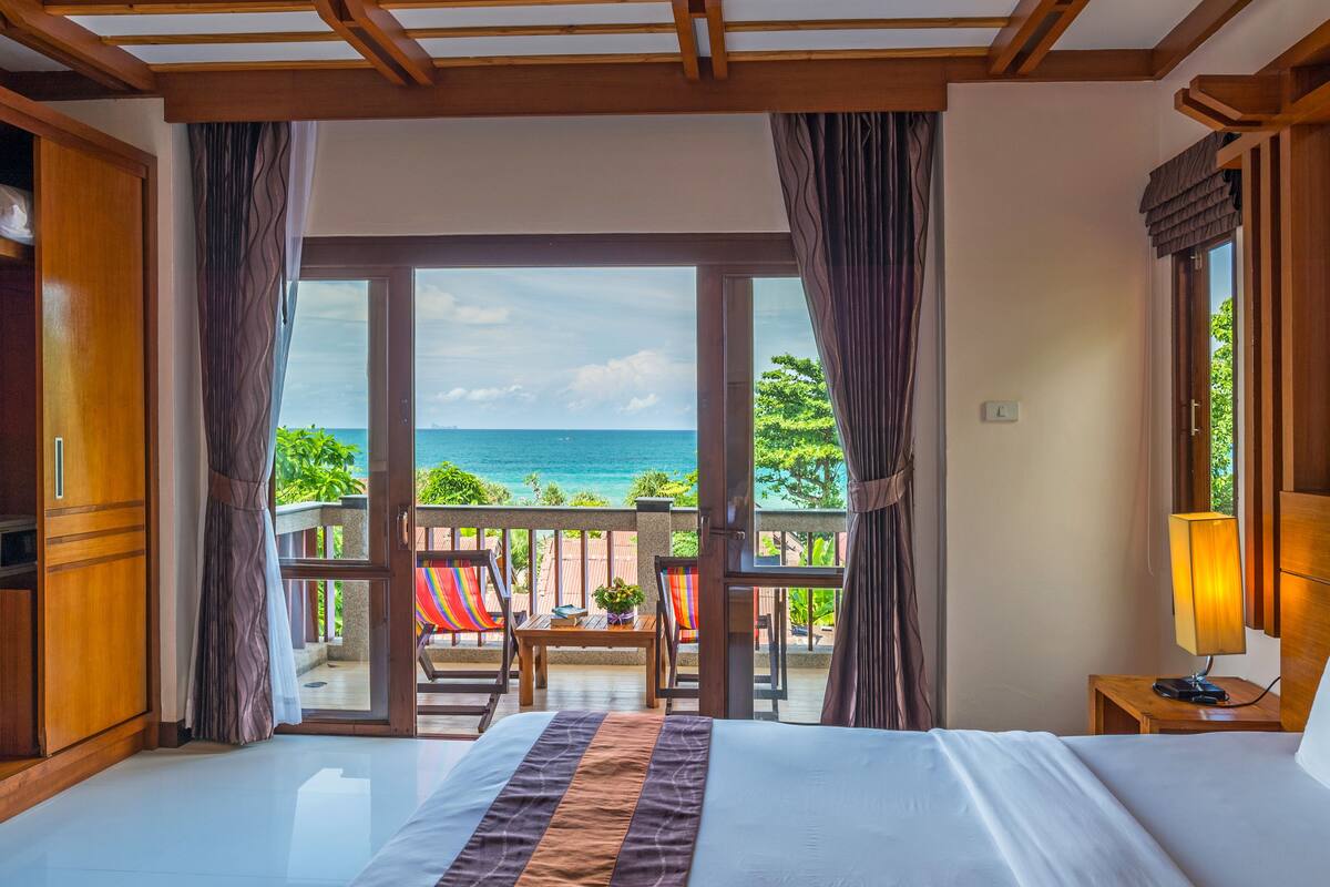 A hotel room with a bed, a nightstand, a lamp, and a view of the ocean.