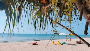 Una playa con una palmera, un flotador salvavidas y sombrillas.