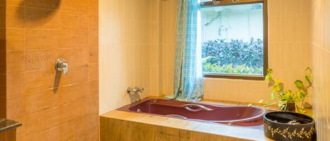 Un baño con techo de madera, una bañera, una ventana con vistas y suelo de baldosas con piedrecitas.