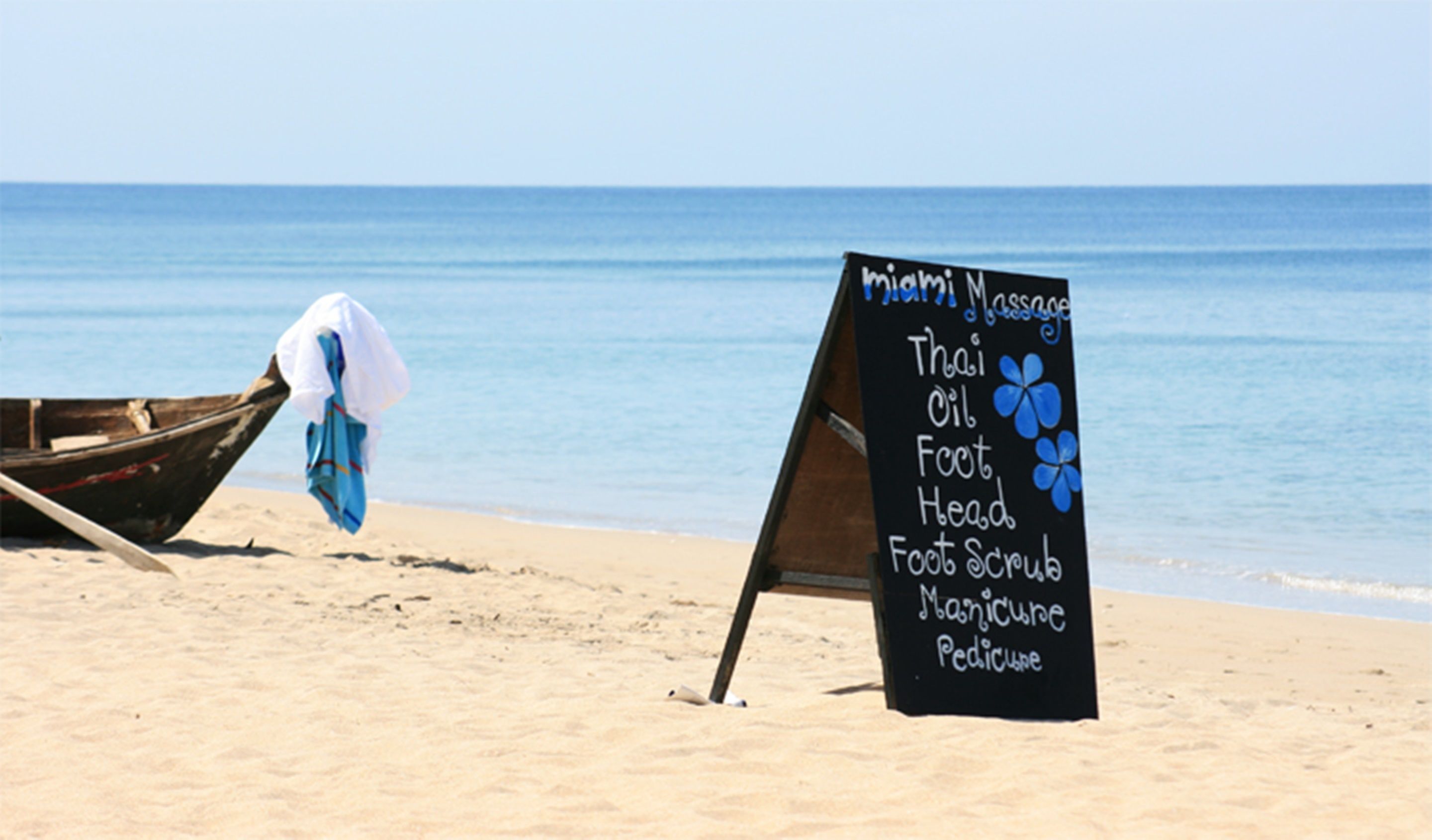 A beach with a sign listing services like Thai massage and foot scrub.