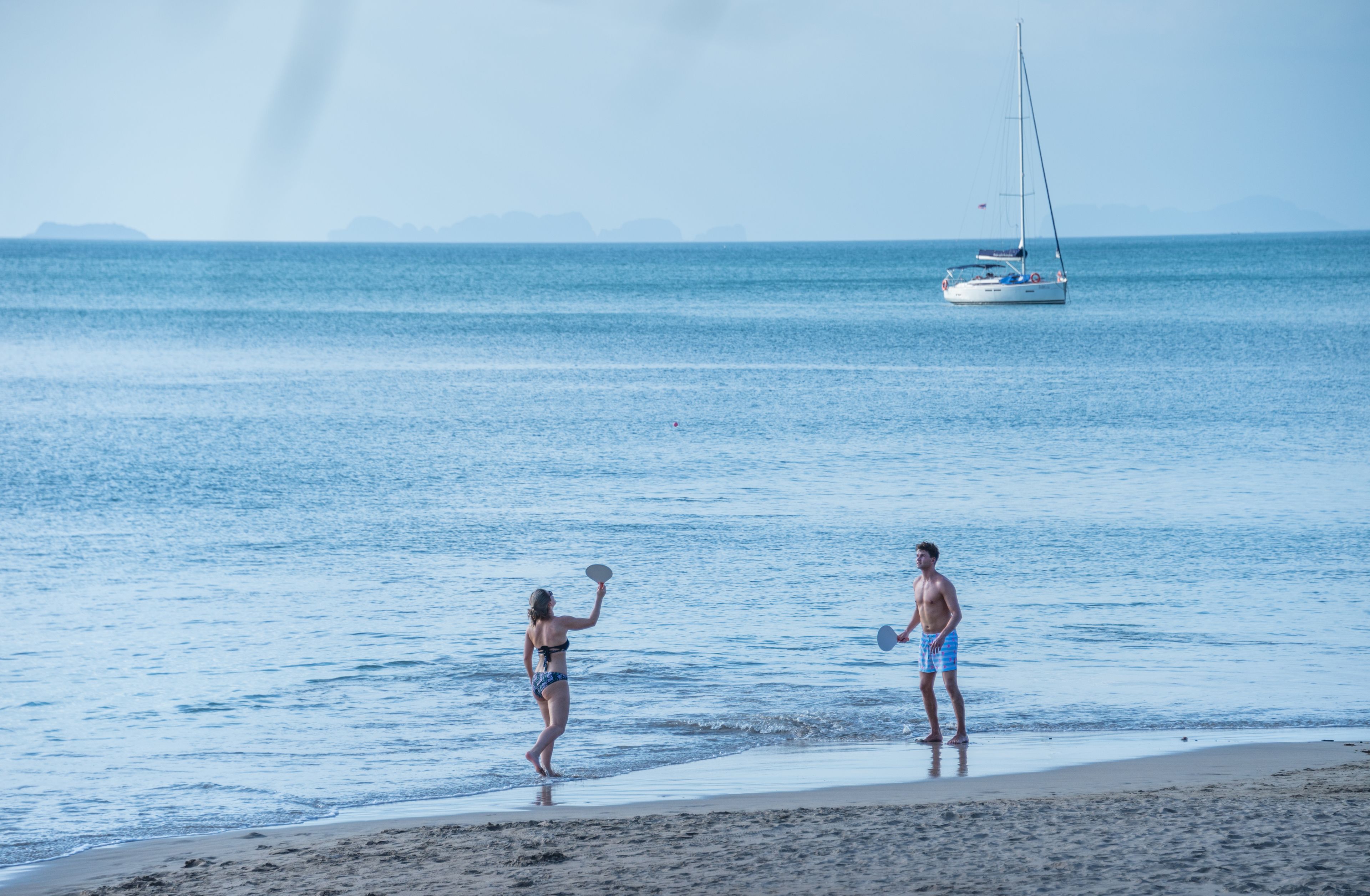 A beach scene with a sailboat in the distance.