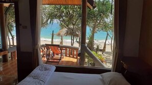 Una habitación con cama y vista a una playa con palmeras y una estructura de techo de paja.