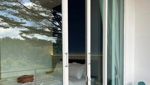 Une chambre avec une porte vitrée donnant sur un balcon, un lit et une chaise.