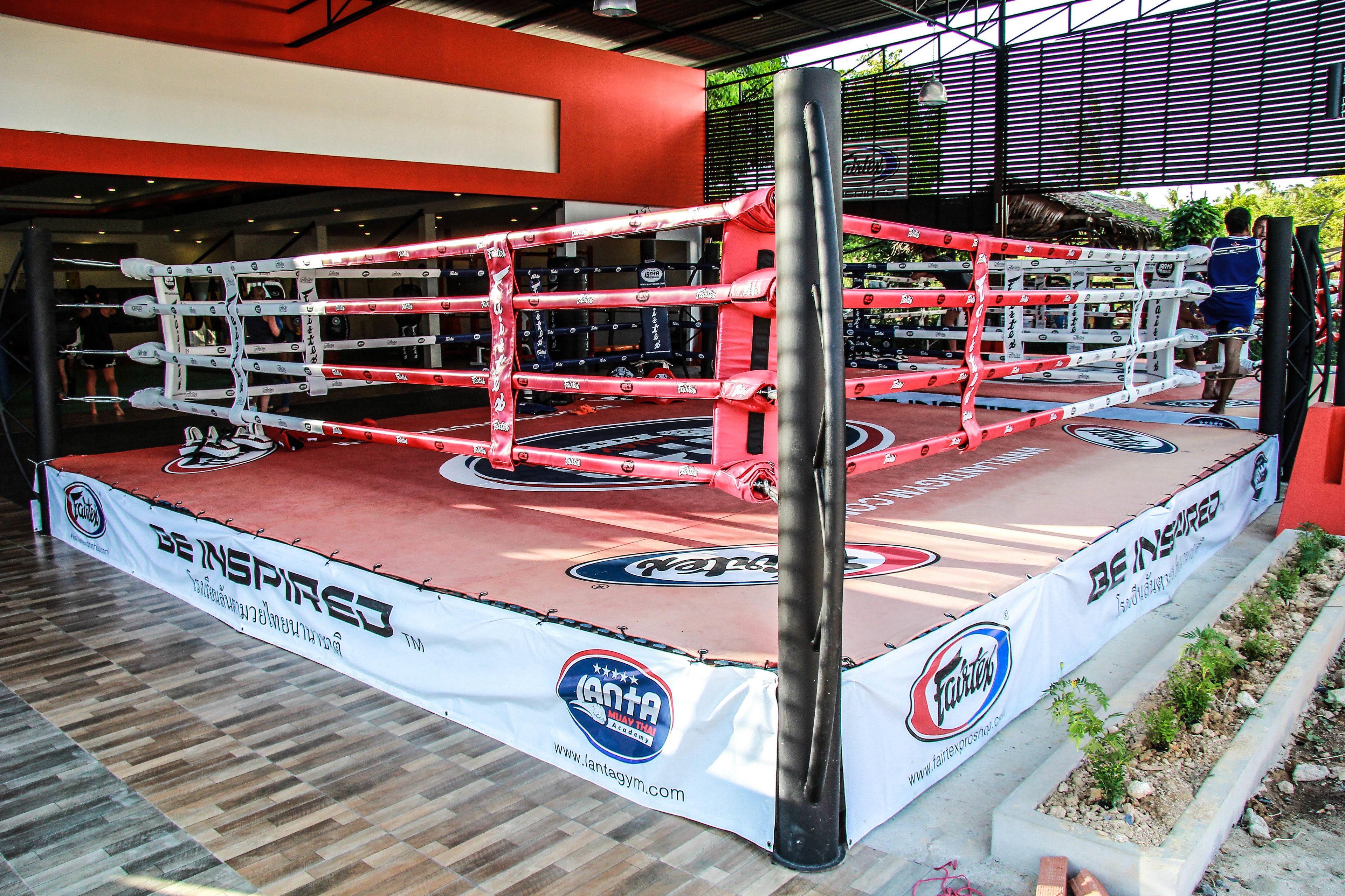 A boxing ring with a wooden floor and a banner with logos and text.