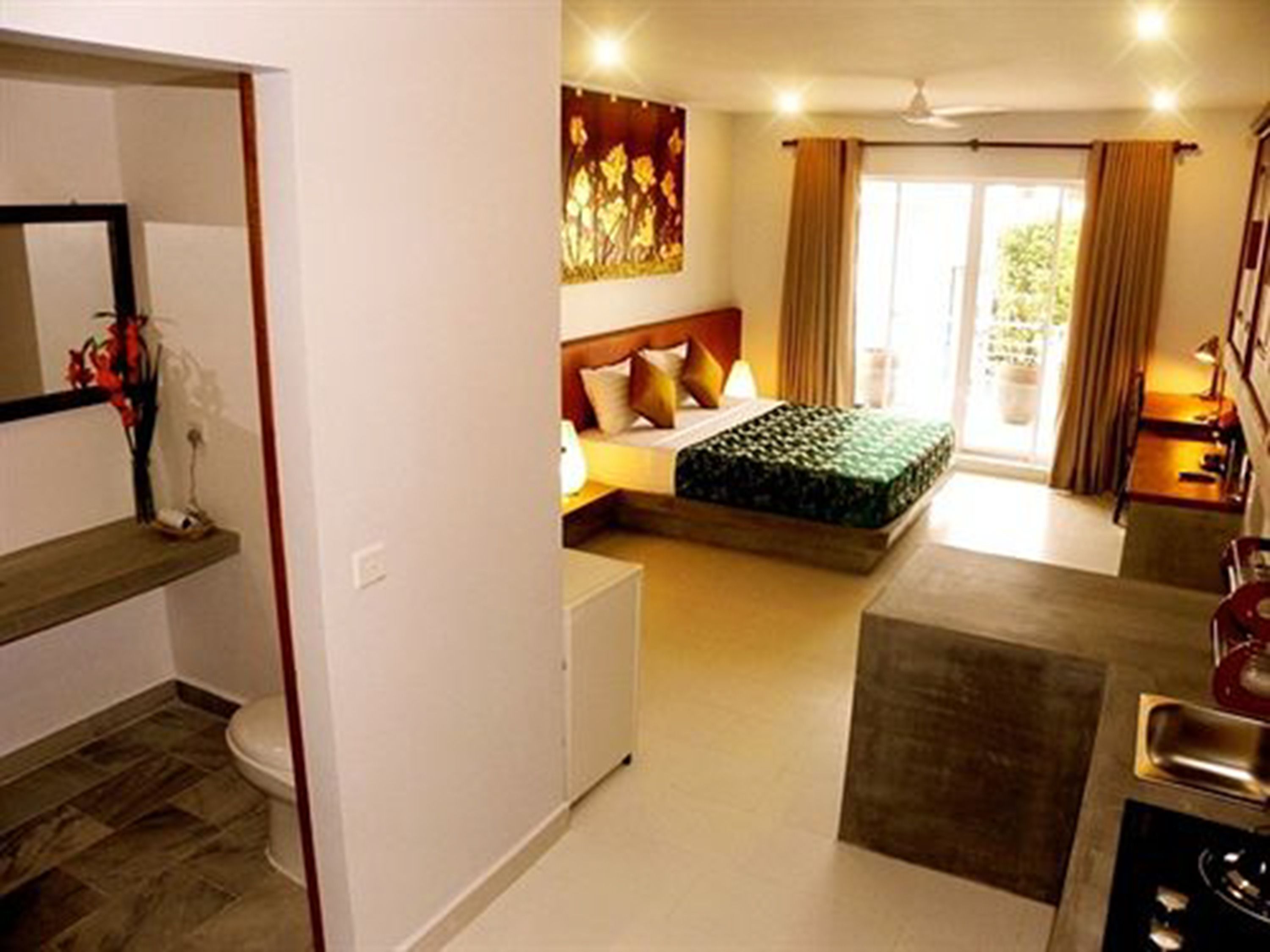 Une chambre à coucher comprenant un lit, une table de chevet, une fenêtre avec des rideaux, ainsi qu’une salle de bain avec des toilettes et un lavabo.