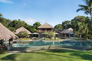 Un resort con piscina, estructuras de techo de paja y abundante vegetación.