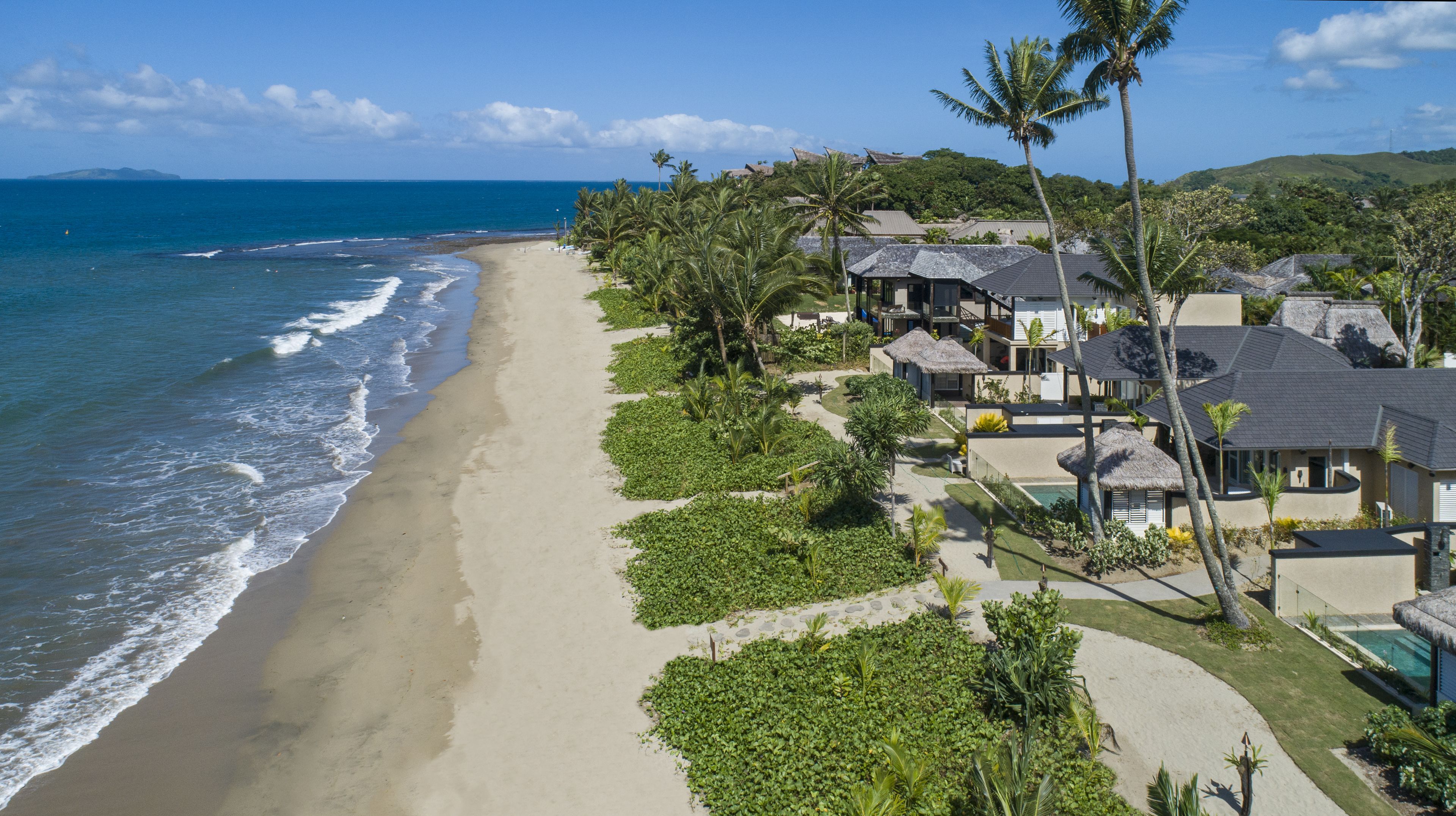 A beachfront property with multiple villas, a sandy beach, and a clear view of the ocean.