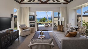 A spacious living room with a large TV, comfortable seating, a coffee table, and a view of the ocean through large windows. - Nanuku Resort Fiji (Pacific Harbour)
