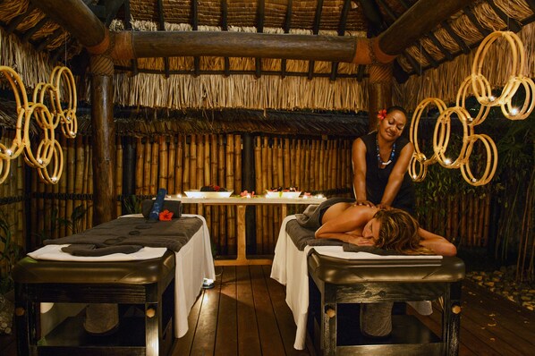 A room with two massage tables, a bamboo wall, and a thatched roof. - Nanuku Resort Fiji (Pacific Harbour)