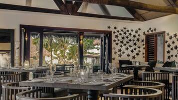 Un restaurante con mesas redondas, sillas de madera oscura y un techo alto con vigas a la vista.