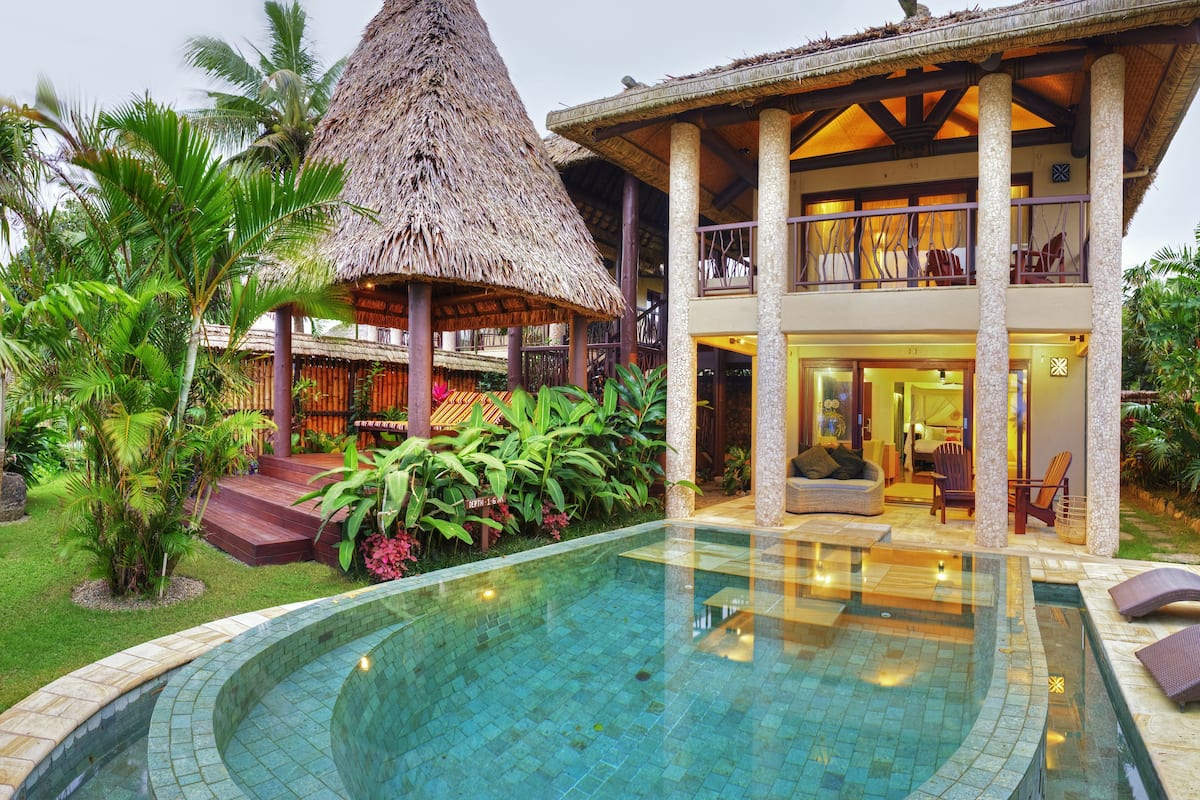 A resort with a swimming pool, a thatched-roof structure, and lush greenery.