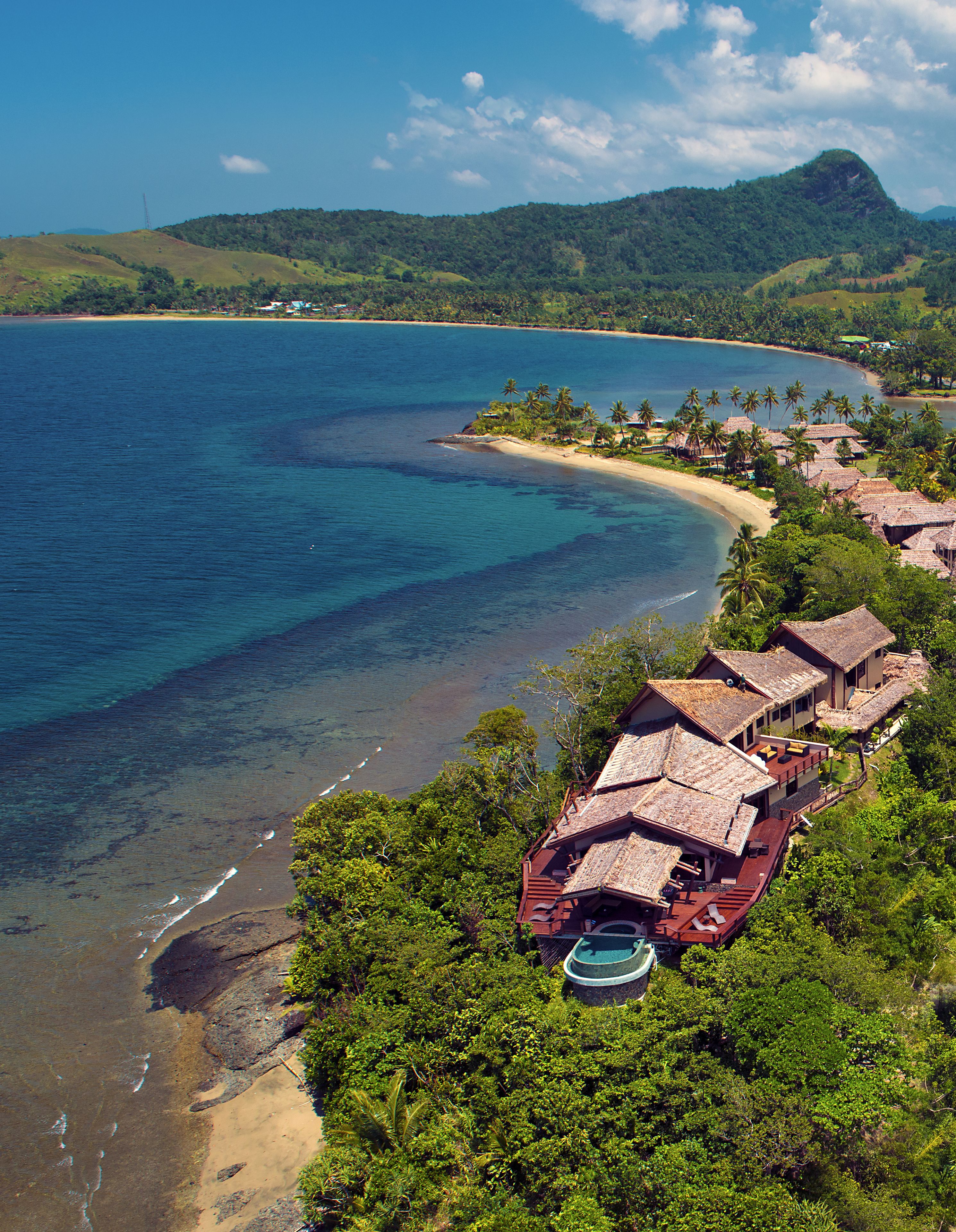 A coastal resort with multiple bungalow-style buildings, a beach, and lush greenery.