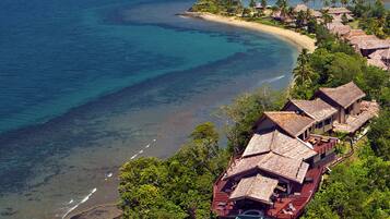 A coastal resort with multiple bungalow-style buildings, a beach, and lush greenery.