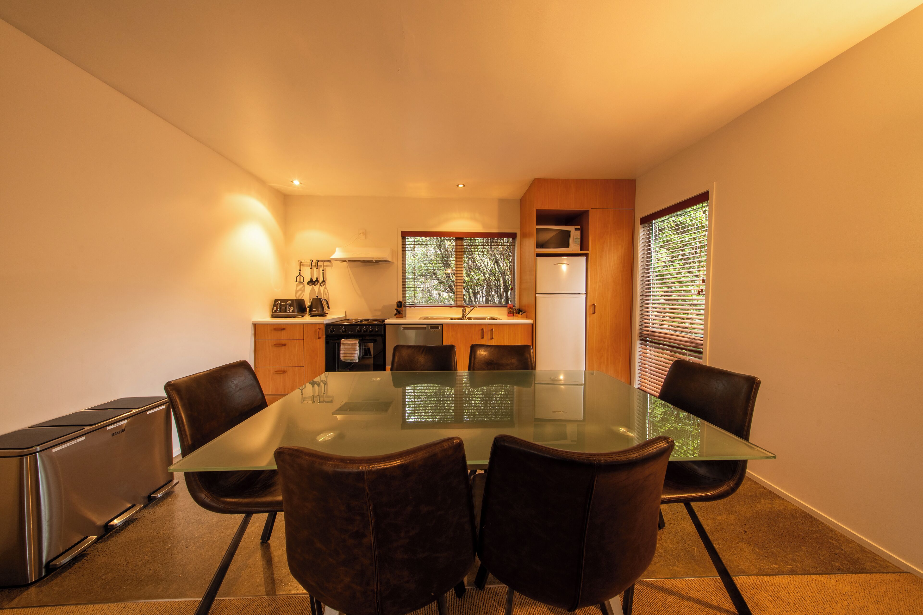 A compact kitchen with a dining area, including a glass-top table and leather chairs.