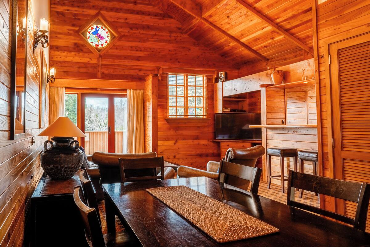 L’intérieur d’un chalet en bois chaleureux et accueillant, avec un coin repas, un téléviseur et un vitrail.
