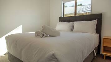 A neatly made bed with a rolled towel, a headboard, and a nightstand with a drawer.
