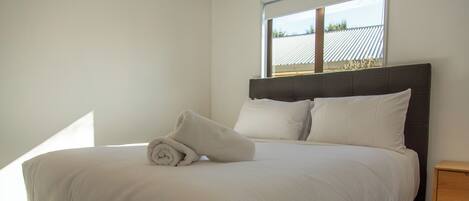 A neatly made bed with a rolled towel, a headboard, and a nightstand with a drawer.