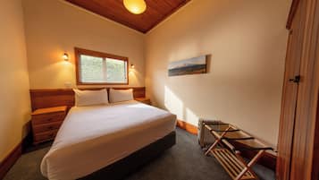 Ein Schlafzimmer mit Bett, Holz-Kopfteil, einem Fenster mit Jalousien, einem Heizkörper und einem Bild an der Wand.