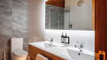A modern bathroom with two sinks, a toilet, and a shower.