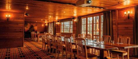 A large wooden dining room with a long table and chairs, large windows, and a patterned floor.
